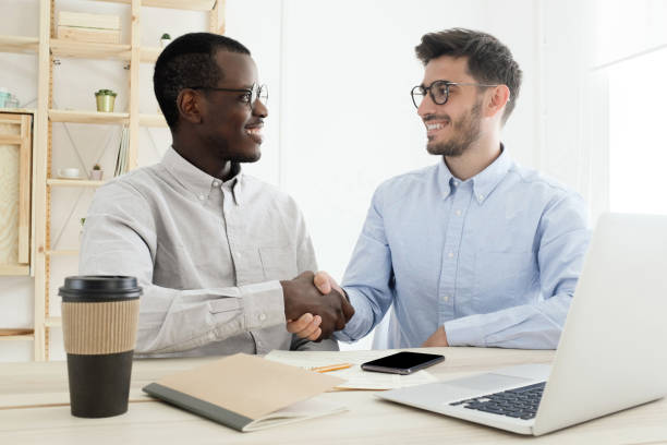 istock Two colleagues in office shaking hands sitting at desk and working together on some project 1183791755