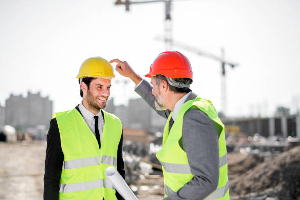 istock Young and senior engineer holding blueprint on construction site 1183797040