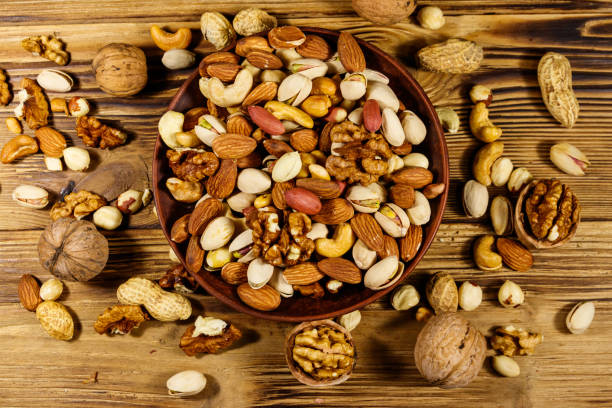 istock Mixed nuts on wooden table. Walnuts, pistachio, almond, peanut, cashew, hazelnut in ceramic bowl. Healthy eating concept. Top view 1183797724