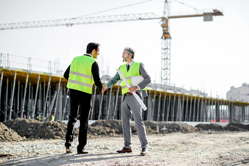 Young and senior engineer shaking hands on construction site