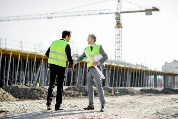 Young and senior engineer shaking hands on construction site stock photo