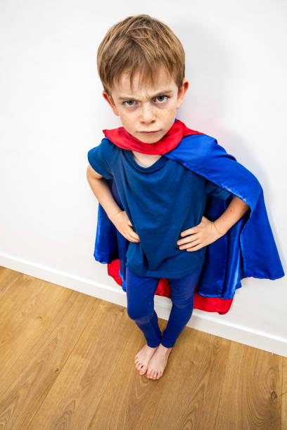 angry superhero child being irritated by denigrating education, white background angry superhero child with hands on hips being irritated, offended, outraged by a denigrating education, white background denigrate stock pictures, royalty-free photos & images