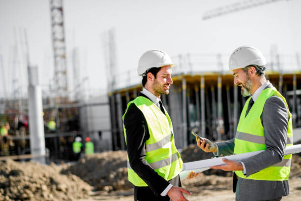 istock Young and senior engineer holding blueprint and phone on construction site 1183801515