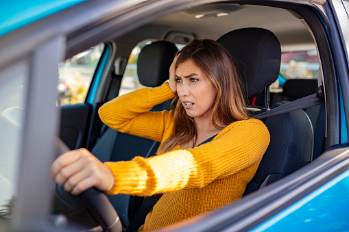 Nervous female driver sits at wheel, has worried expression as afraids to drive car by herself for first time. Frightened woman has car accident on road. People, driving, problems with transport