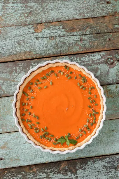 Bright orange pumpkin pie with pumpkin,  flax and amaranth seeds on blue background top view copy space