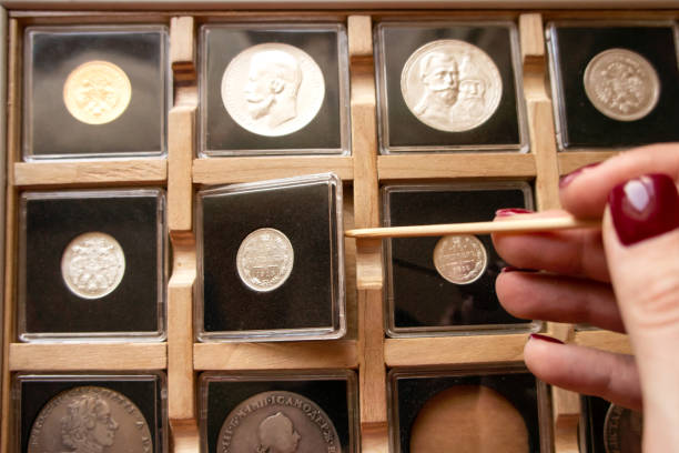 female hand taking out a coin from a wooden display case with numismatic collection with a wooden stick. coin holder case with plastic protection square capsules - coin collection imagens e fotografias de stock