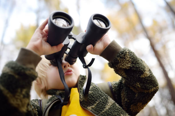 pequeño boy scout con binoculares durante el senderismo en el bosque de otoño. el niño está mirando a través de los prismáticos. - discovery binoculars boy scout searching fotografías e imágenes de stock