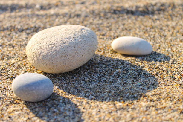 istock Three white pebble stones on the sand. Sunset photo with long shadows. 1183814898