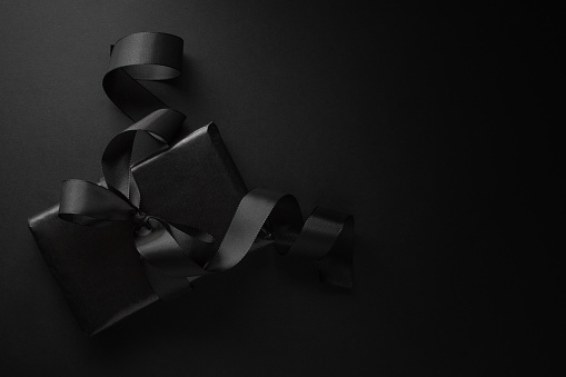 Gift wrapped in black paper with black bow on dark background. View from above.