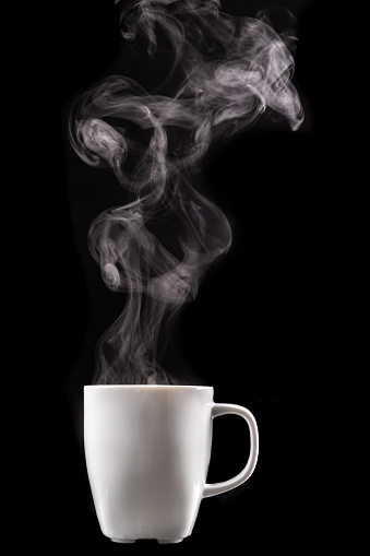 A white mug of warm drink and steam. Tasty hot coffee on a dark table. Black background.