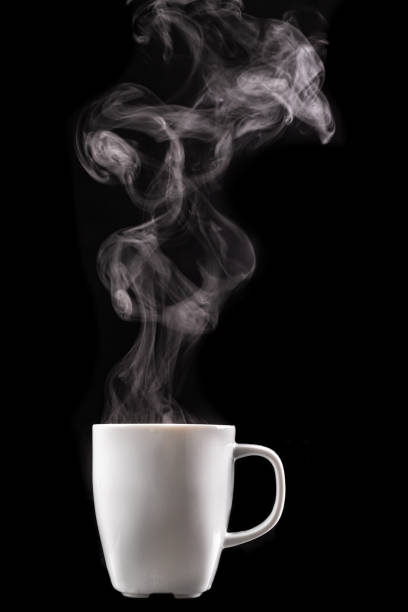 A white mug of warm drink and steam. Tasty hot coffee on a dark table. Black background. A white mug of warm drink and steam. Tasty hot coffee on a dark table. Black background. steam stock pictures, royalty-free photos & images