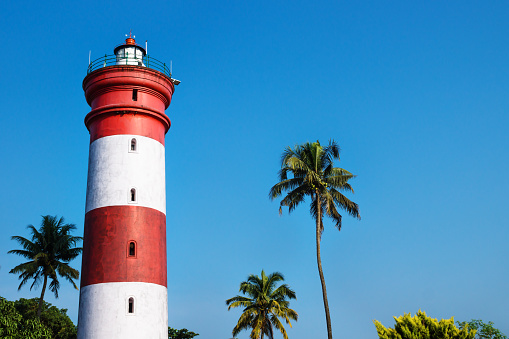 Alleppey Lighthouse with red and white stripes with palm trees on cloudless blue sky, Aleppuzha, Kerala, India