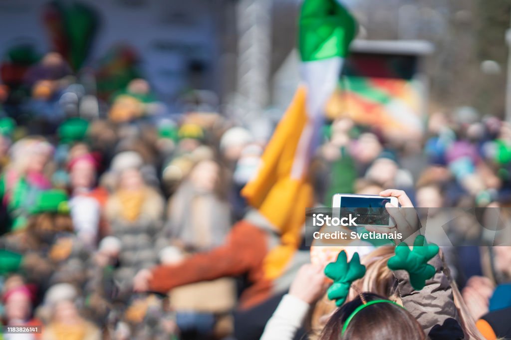Hands of girl with mobile phone, making photo of carnival of St. Patrick's Day, traditional carnival party on a smartphone Hands of girl with mobile phone, making photo, video of carnival of St. Patrick's Day, traditional carnival party on a smartphone St. Patrick's Day Stock Photo
