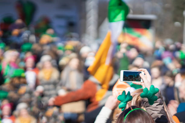 hands of girl with mobile phone, making photo of carnival of st. patrick's day, traditional carnival party on a smartphone - carnival parade imagens e fotografias de stock