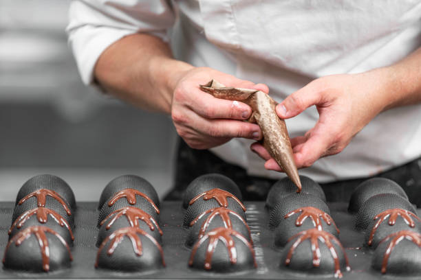 istock Making handmade chocolates. A confectioner pours liquid dark chocolate into molds. Close-up. 1183832344
