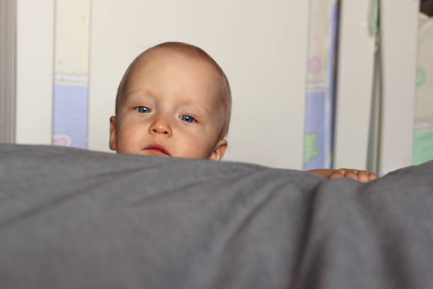 istock Curiosity. A curious baby's face peeks out over the bed. Education, interest, emotions. Face close up. 1183846456
