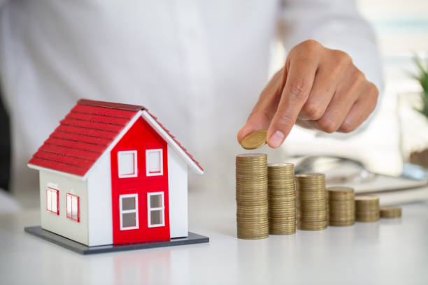 istock Woman's hand putting house model on coins stack. Concept for property ladder, planning savings money of coins to buy a home concept property mortgage and investment for a house. 1183854794