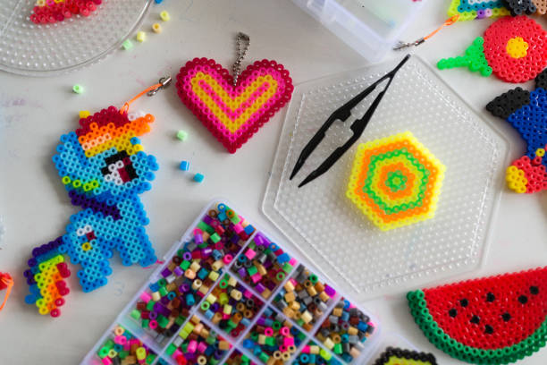 Cute little girl makes a toy with thermo mosaic. Development, modeling, education, design with hot plastic indoor. Modern technologies. DIY. Flat lay, top view, overhead