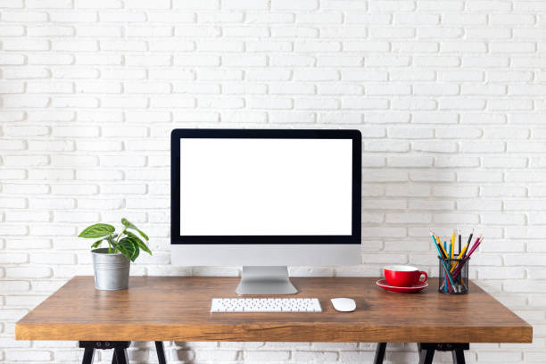 istock Mockup blank screen computer on a wooden desk. desktop empty white screen, with workspace and office supplies on table 1183870229
