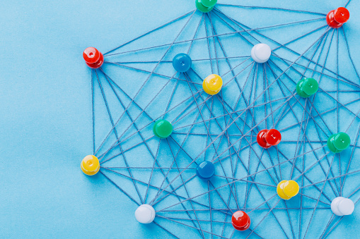 Small network of pins (Thumbtack)and string, An arrangement of colorful pins linked together with string on a pale blue background suggesting a network of connections.