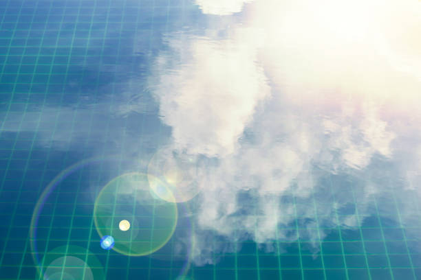 Flat water surface in blue tiles floor of  swimming pool with bokeh lens flare and white cloud reflection used for background ,high angle view.\nCloud reflection  in the pool with copy space.