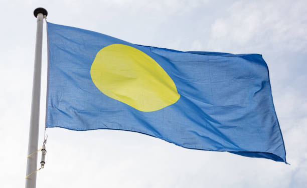 Palauan flag waving against cloudy sky background Palau flag. Palauan national sign and symbol waving on a flagpole against cloudy sky background palau stock pictures, royalty-free photos & images