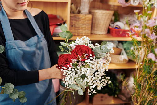 Female florist showing beautiful bouquet with red roses, gypsophila and eucalyptus