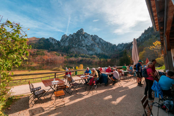 randonneurs et touristes assis au soleil à la terrasse de l'aumône ramsauer et profitant de la vue sur le laudachsee et la paroi rocheuse de katzenstein - mountain rock sun european alps photos et images de collection