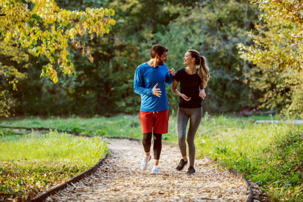 pleine longueur de couples caucasien mignons dans des vêtements de sport marchant sur le sentier dans les bois, souriant et parlant - power walking photos et images de collection