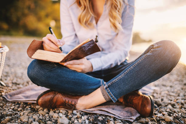 cropped picture of focused fashionable beautiful caucasian woman sitting near river and holding notebook. - sky human hand water white imagens e fotografias de stock