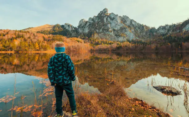 Gmunden, Austria - October 24th 2019: Beautiful landscape enclosed by Traunstein, Katzenstein and the Grünberg mountain. Boy standing at the water's edge.