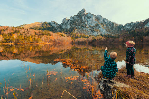 małe dzieci na brzegu laudachsee, austria, z oszałamiającym katzenstein rośnie w tle i odbija się w krystalicznie czystej wodzie - european alps austria autumn colors zdjęcia i obrazy z banku zdjęć