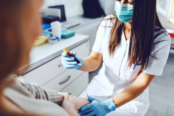 Female lab assistant in uniform, with protective mask and rubber gloves holding test tube with blood and holding patient's arm. Patient holding cotton on vein. Female lab assistant in uniform, with protective mask and rubber gloves holding test tube with blood and holding patient's arm. Patient holding cotton on vein. donors choose stock pictures, royalty-free photos & images