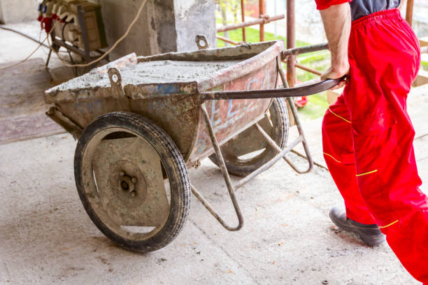 Construction worker is using his manpower to manage wheelbarrow with fresh mortar at construction site.