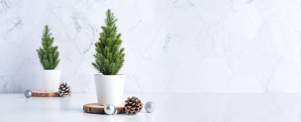 christmas tree with pine cone,decor xmas ball on wood log at white table and marble tile wall background.clean minimal simple style.holiday still life with space to adding text