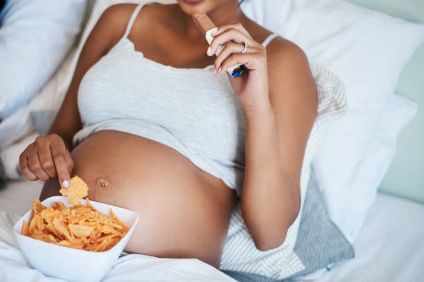 Just remember I'm eating for two okay Cropped shot of unrecognizable pregnant woman eating potato chips and chocolate in bed family eating potato chips stock pictures, royalty-free photos & images