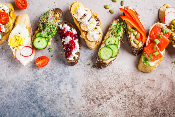 istock Open toasts with different toppings on gray-brown background, copy space, top view.  Flat lay of crostini with banana, pate, avocado, salmon, egg, cheese and berries. 1183916918