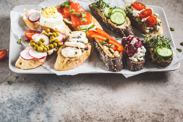 istock Open toasts with different toppings on gray-brown background. Crostini with banana, pate, avocado, salmon, egg, cheese and berries. 1183917009