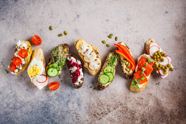 istock Open toasts with different toppings on gray-brown background, copy space, top view.  Flat lay of crostini with banana, pate, avocado, salmon, egg, cheese and berries. 1183917137