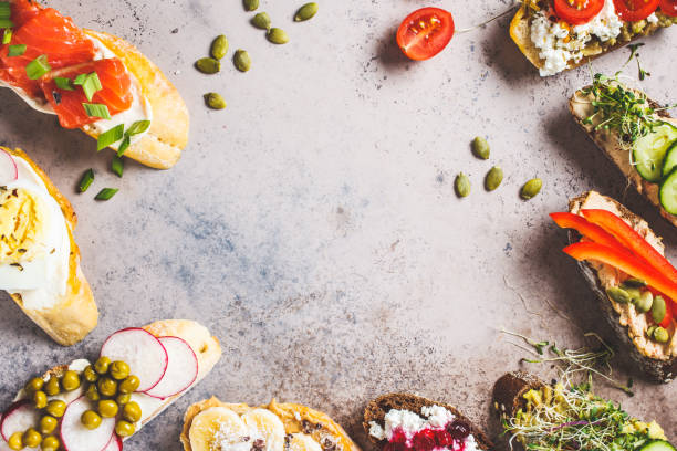 istock Open toasts with different toppings on gray-brown background, copy space, top view.  Frame of crostini with banana, pate, avocado, salmon, egg, cheese and berries. 1183917662
