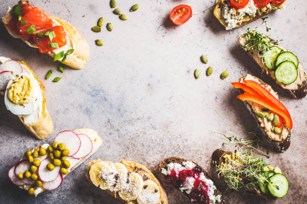 istock Open toasts with different toppings on gray-brown background, copy space, top view.  Frame of crostini with banana, pate, avocado, salmon, egg, cheese and berries. 1183917692