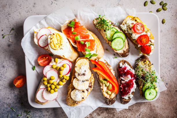 istock Open toasts with different toppings on gray-brown background.  Crostini with banana, pate, avocado, salmon, egg, cheese and berries. 1183917736