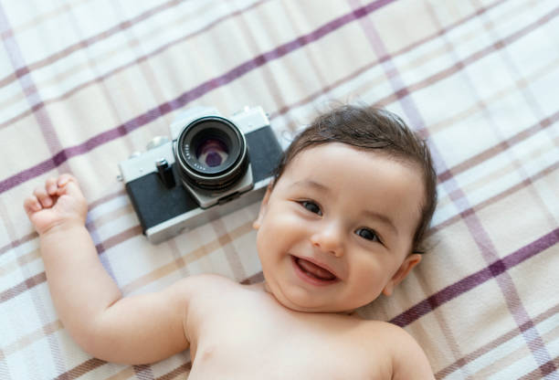Baby boy lying on bed with SLR Camera