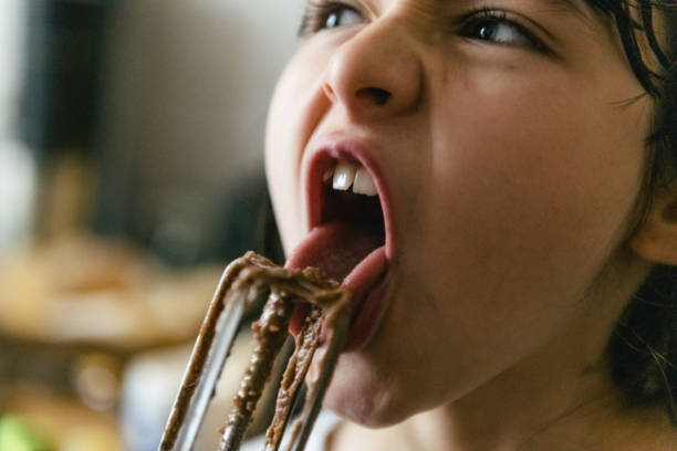 portrait of little girl licking blender with chocolate dough