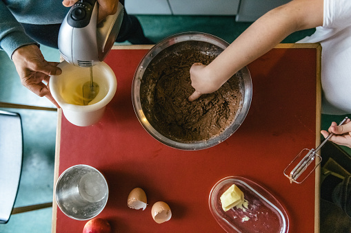 overhead view on little girl and mother preparing together  dough for chocolate cake in kitchen