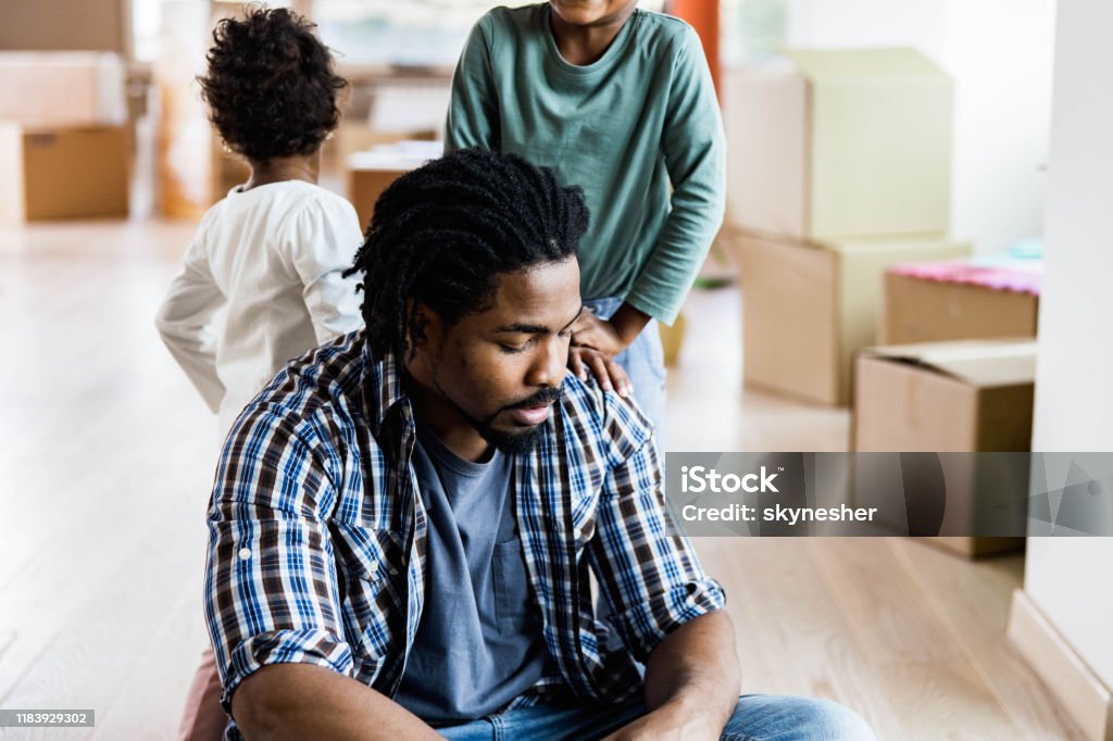 Worried African American single father with his kids at new apartment. Young black father feeling sad after relocating into new home with his kids. Sadness Stock Photo