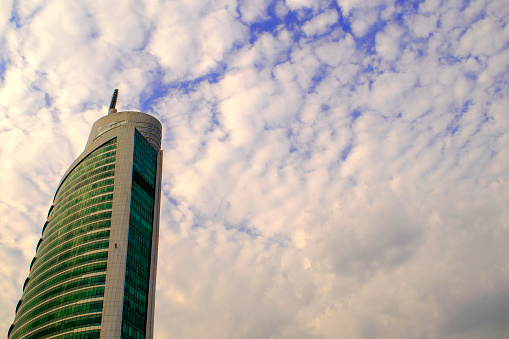 Dubai / United Arab Emirates - September 01, 2019: Upper part of skyscraper Almas Tower business center on blue fluffy sky background