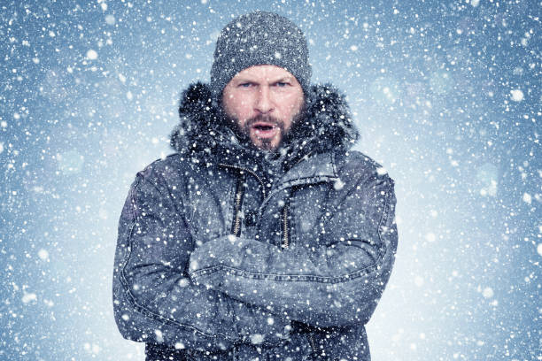 Frozen bearded man in a sheepskin coat and hat warms his hands, cold, snow, frost, blizzard Frozen bearded man in a sheepskin coat and hat warms his hands, cold, snow, frost, blizzard warms stock pictures, royalty-free photos & images