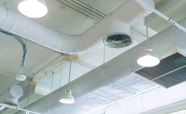 Photo of Air duct, air conditioner pipe and fire sprinkler system on white ceiling wall. Air flow and ventilation system. Building interior. Ceiling lamp light with opened light. Interior architecture concept.