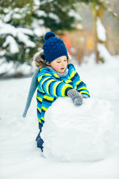 istock little cute boy making snowman. rolling big snowball. winter leisure 1183938122